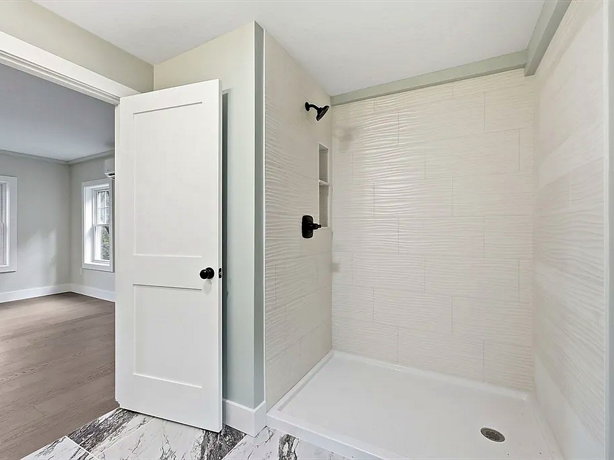 Textured wall tile in a shower, marble-look tile floor, hardwood in the adjoining room